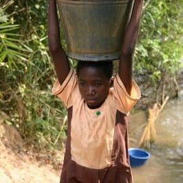 Teen boy carrying water barrel over head
